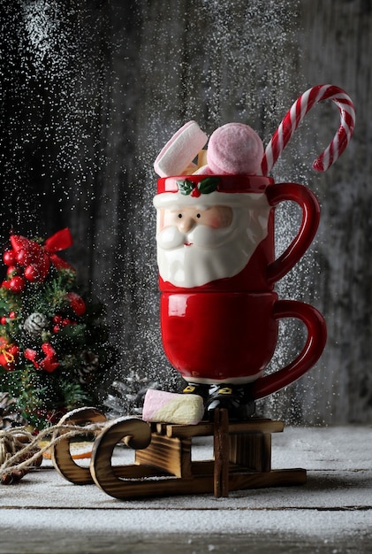 taza de santa llena de malvaviscos y caramelos sobre trineo de madera