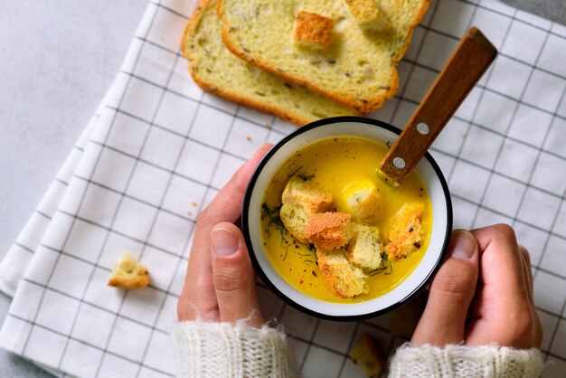 Taza con sopa de crema de zanahoria en manos de niña