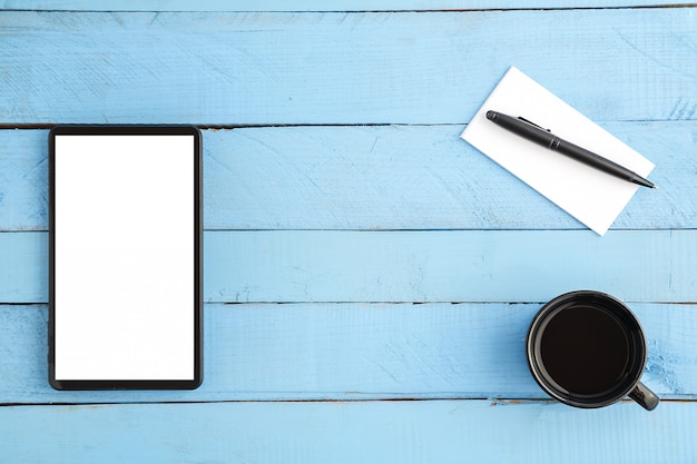 taza, tableta, libreta de papel pequeña y un bolígrafo negro sobre madera azul