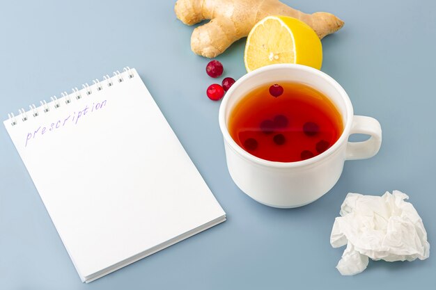 Taza de té con arándanos, limón, servilleta arrugada, mascarilla médica y receta en azul