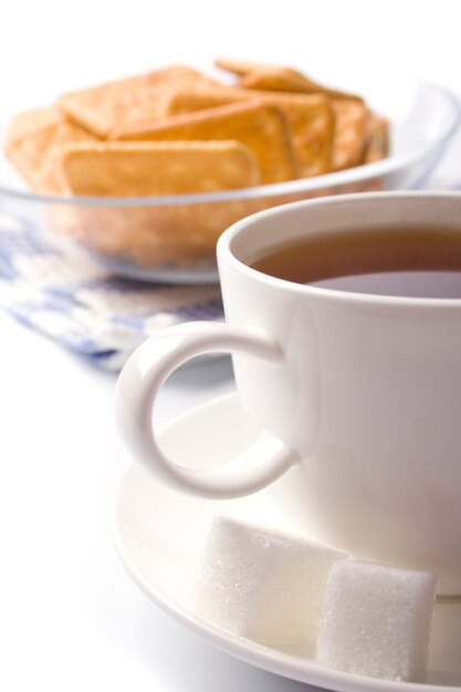 Taza de té, azúcar y galletas closeup en blanco