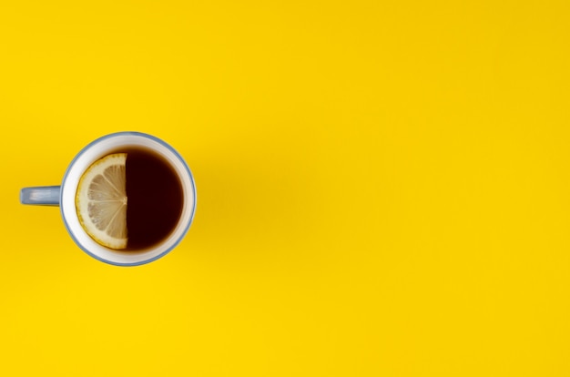 Taza de té azul con composición de rodaja de limón sobre fondo amarillo.