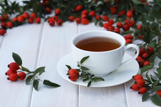 Taza de té con bayas de rosa sobre un fondo blanco de madera