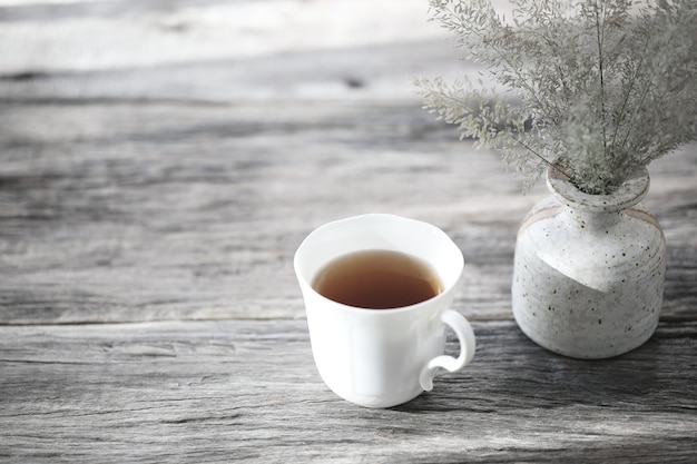 Taza de té blanco con maceta de flor seca sobre mesa de madera rústica