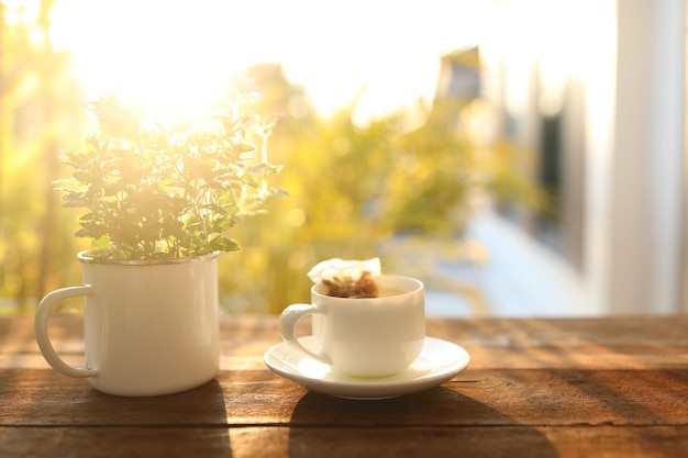 Taza de té blanco y maceta de Verbena, mesa de madera, balcón con luz natural