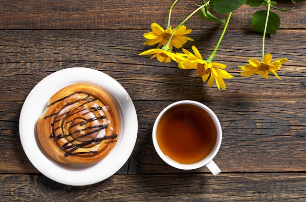 Taza de té y bollo dulce en mesa de madera con flores