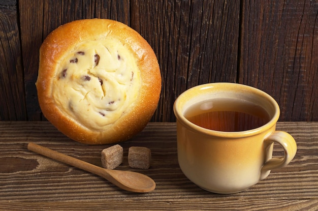 Taza de té y bollo con requesón y pasas para desayunar en una mesa de madera oscura