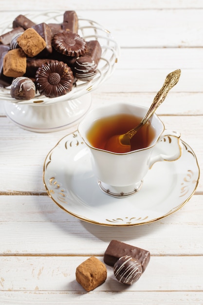 Taza de té con bombones en mesa de madera blanca