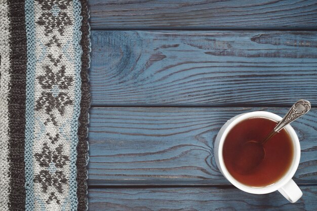 Una taza de té y una bufanda tejida en el fondo de la mesa de madera azul