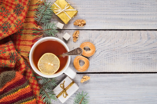 Una taza de té, una bufanda tejida y regalos en el fondo de la mesa de madera blanca