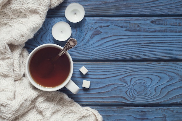 Una taza de té, una bufanda tejida y velas en el fondo de la mesa de madera azul