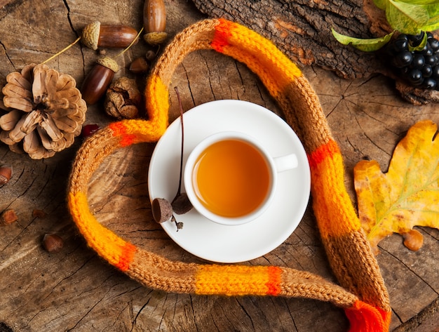 Taza de té caliente con una bufanda sobre fondo de madera