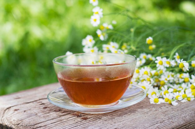 taza de té caliente con flores de manzanilla en la mesa de madera en el jardín de verano