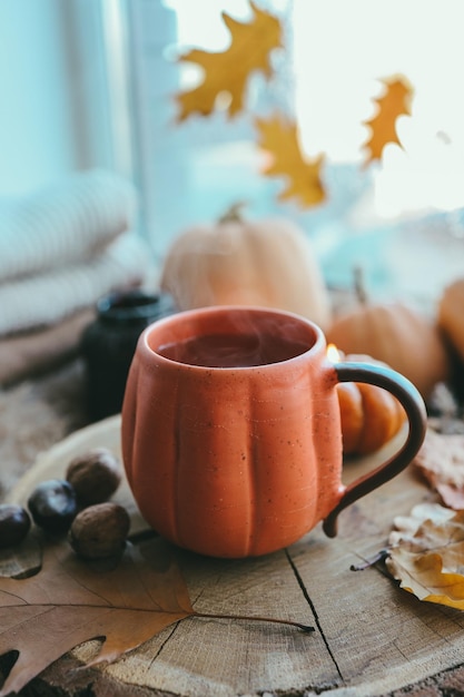 Una taza de té caliente y humeante y una vela en forma de calabaza en el alféizar de la ventana