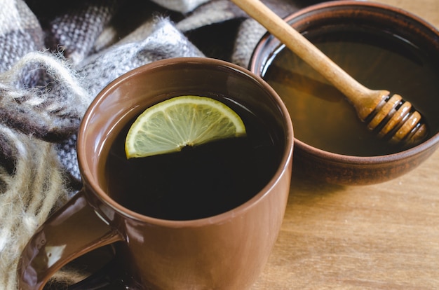 Una taza de té caliente con limón, miel y plaid.