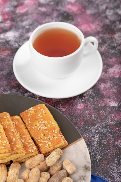 Taza de té caliente con maní saludable con cáscara y galletas.