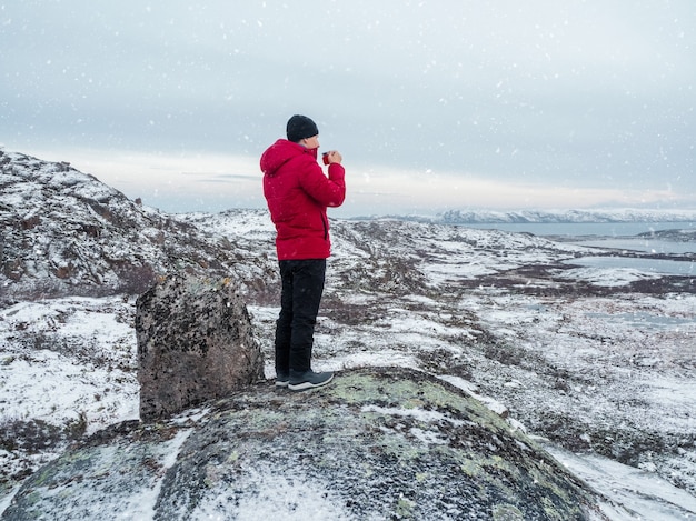 Una taza de té caliente en la mano de un hombre en la cima de una colina polar. colinas del norte cubiertas de nieve. Maravilloso paisaje polar. El concepto de viaje.