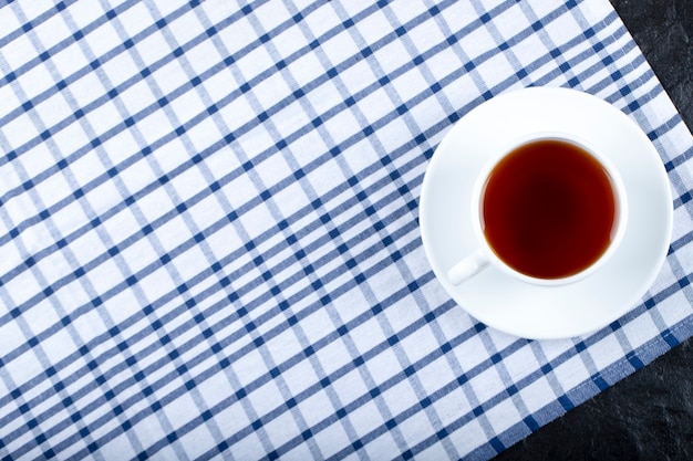 Taza de té caliente con mantel azul sobre negro.