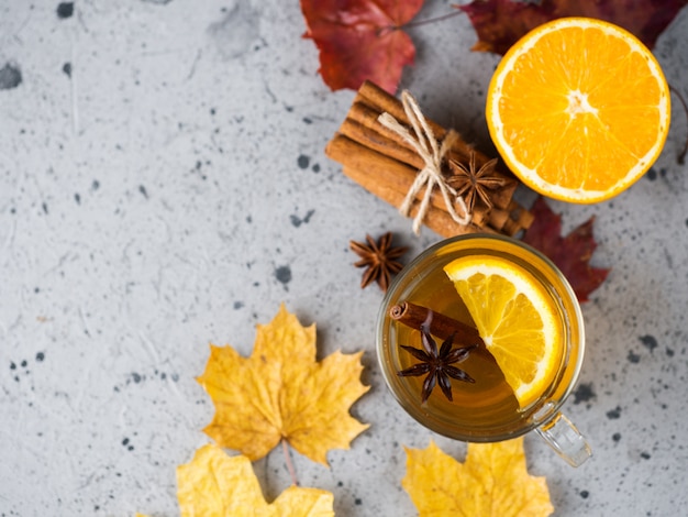 Una taza de té caliente con naranja y canela sobre una mesa de piedra con hojas secas de otoño