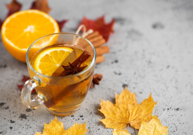 Una taza de té caliente con naranja y canela sobre una mesa de piedra con hojas secas de otoño