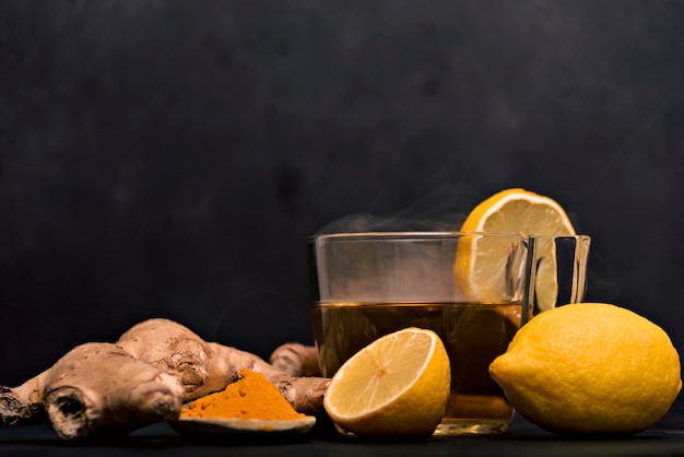 Taza de té caliente con raíz de jengibre, limón y cúrcuma agregando miel cruda natural a una taza de vitamina de té caliente