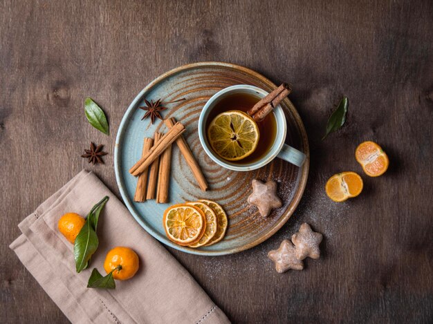 Una taza de té caliente con rodajas de mandarina seca y palitos de canela sobre un fondo de madera