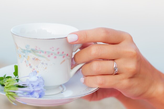 Taza de té de cerámica con flores en manos bien cuidadas de mujeres con manicura.