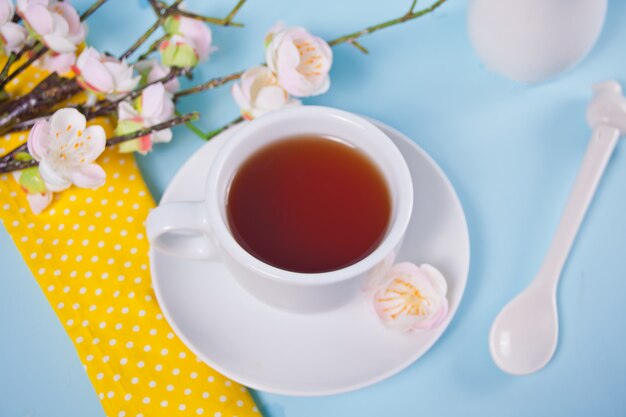 Una taza de té y cereza florece con flores de sakura en la superficie azul. Concepto de primavera.