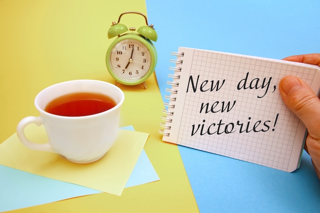 Foto taza de té y un cuaderno con la inscripción new day new victories