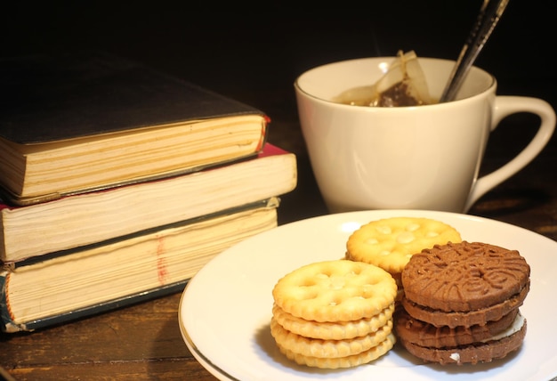 taza de té con cuchara pequeña, galleta en un plato y una pila de libros sobre la mesa enfoque selectivo