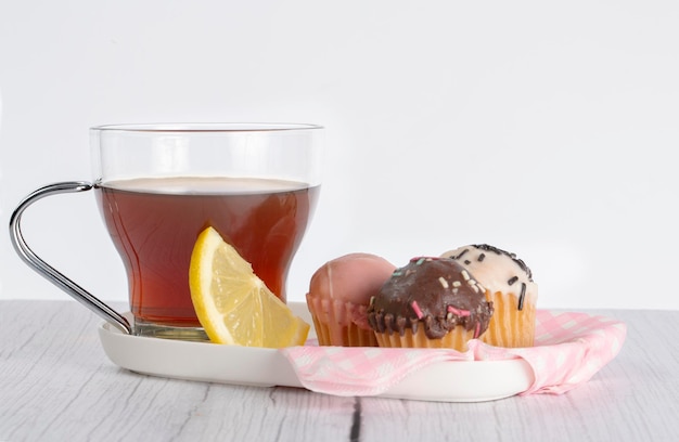 Foto taza de té con cuña de limón acompañada de pequeños cupcakes de variados sabores y colores