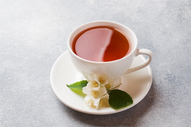 Taza de té con flores de jazmín en una mesa gris