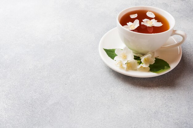 Taza de té con flores de jazmín en una mesa gris