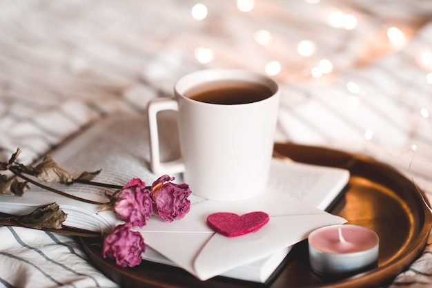 Taza de té con flores en primer plano de libro abierto. Día de San Valentín. Hora de dormir.