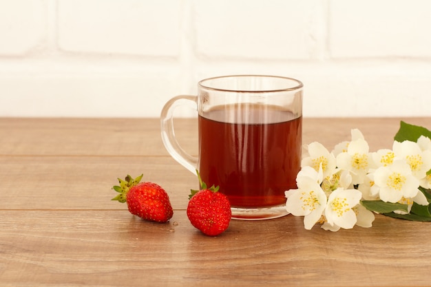 Taza de té con fresas y flores de jazmín blanco sobre escritorio de madera.