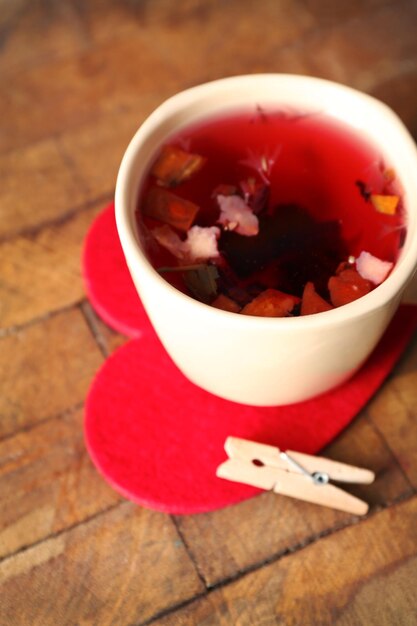 Foto taza de té de frutas en corazón rojo con pinza para la ropa en primer plano de fondo de madera