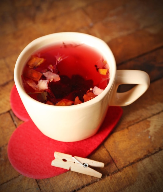 Foto taza de té de frutas en corazón rojo con pinza para la ropa en primer plano de fondo de madera