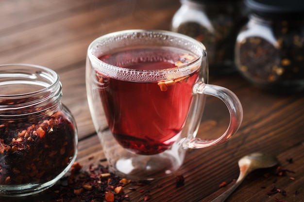 Taza de té de frutas rojas calientes tarro de té de frutas naturales con pétalos de hibisco rodajas de frutas y bayas