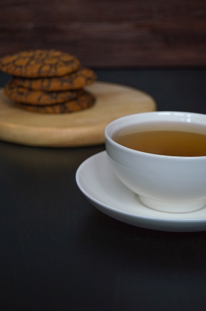 Una taza de té y galletas de avena en un soporte de madera sobre un fondo oscuro