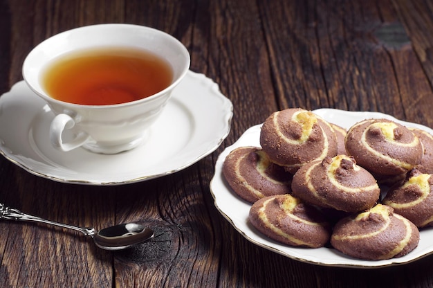 Taza de té y galletas con chocolate en la mesa de madera oscura.