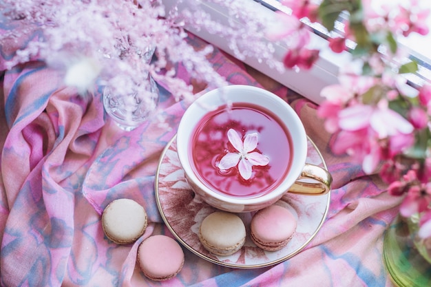 una taza de té con galletas de pasta junto a la ventana junto a las flores