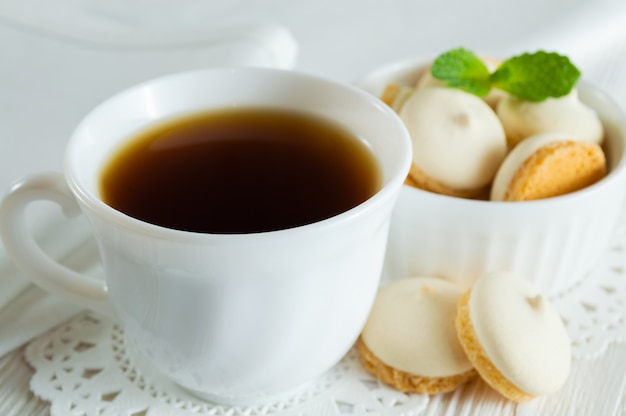 Una taza de té y galletas pequeñas con hojas de menta en una mesa de madera blanca.