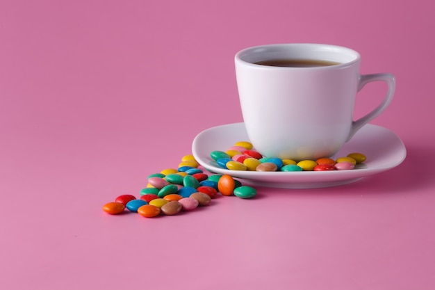 Taza de té con grageas dulces de colores en el plato