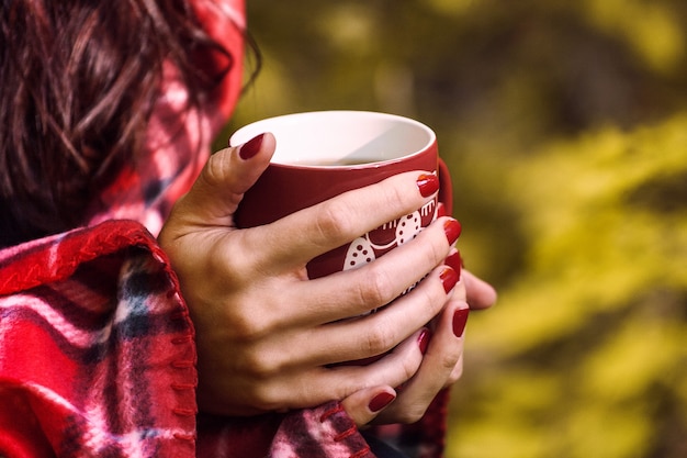 Taza de té de hierbas en manos de mujer. Otoño otoño de cerca, bebida de temporada al aire libre en el bosque.