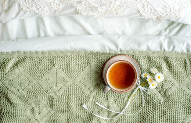 Taza de té de hierbas naturales de menta y bálsamo de limón en la cama, por la mañana de cerca. Ambiente acogedor. Encaje calado, manta de algodón blanco, flores de margaritas de verano. Desayuno. Estilo provenzal y retro.