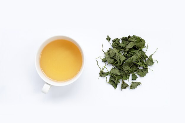 Taza de té con hojas secas de centella asiática sobre fondo blanco.