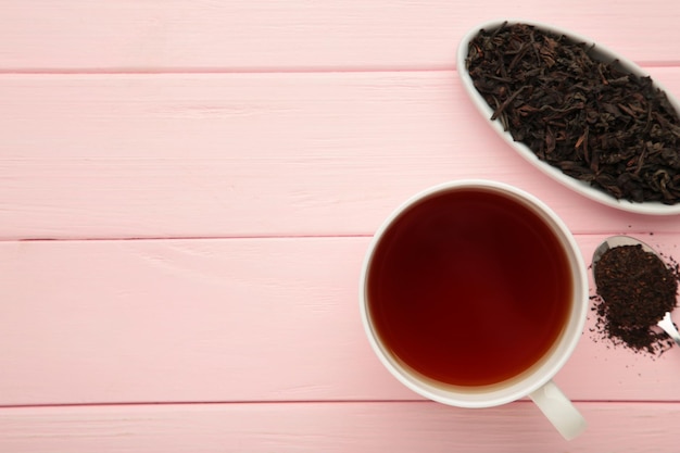 Taza de té con hojas de té secas sobre fondo rosa