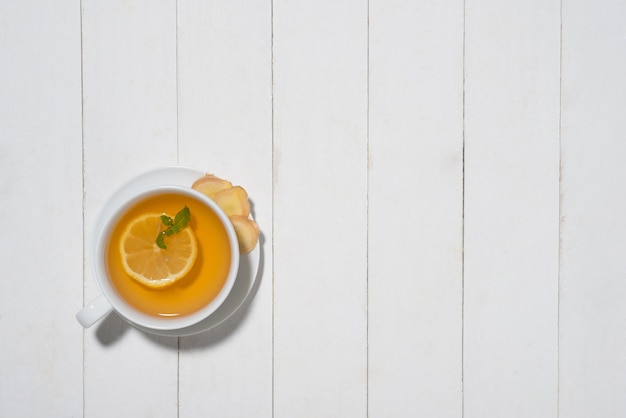 Taza de té de jengibre con limón y miel sobre un fondo de madera blanca.