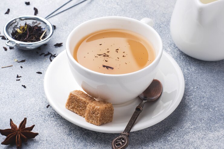 Taza de té con leche, azúcar de anís marrón sobre una mesa gris.
