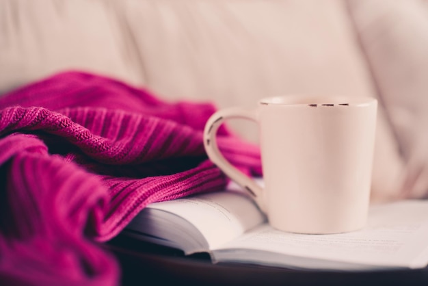 Taza de té en libro abierto con suéter de punto en la cama Buenos días